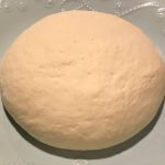 A ball of pizza dough laying on a blue plate.