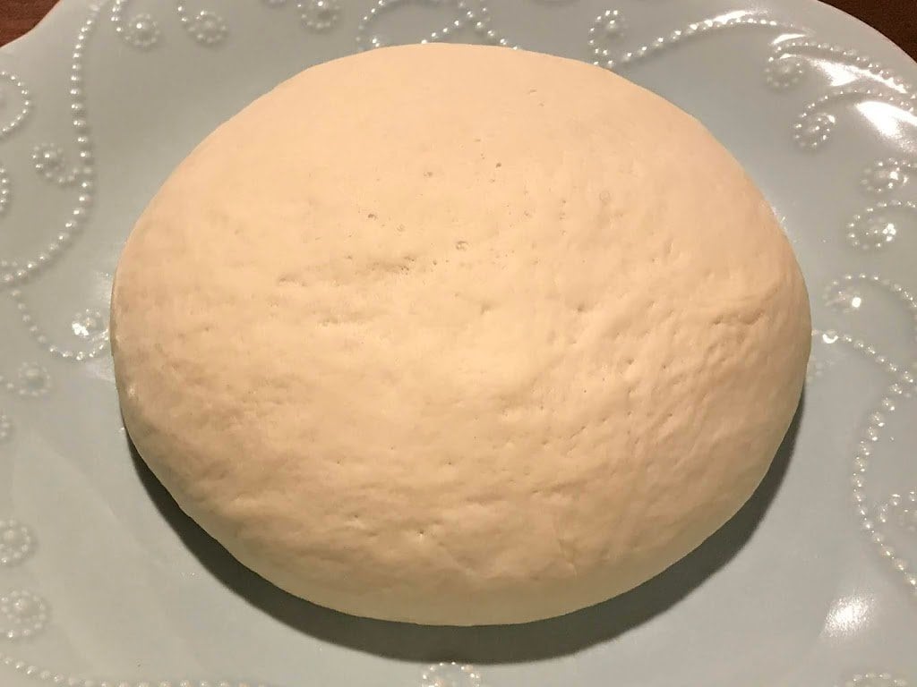 A ball of pizza dough laying on a blue plate.