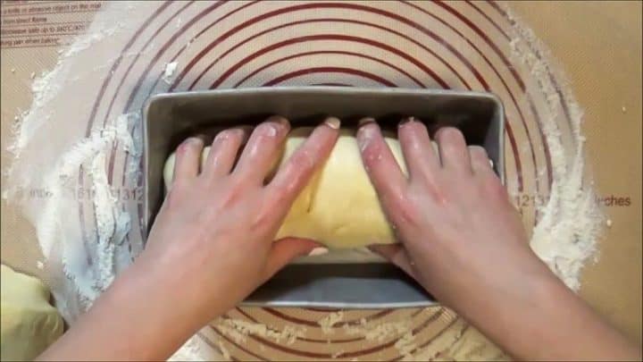 Placing bread dough in greased bread loaf pans for final rise.