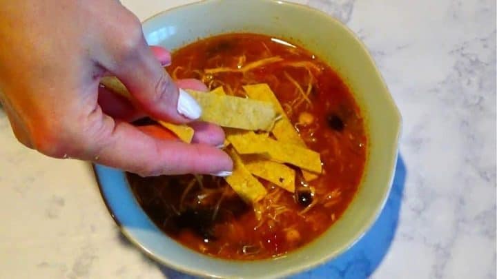 Placing baked tortilla strips in a bowl of chicken tortilla soup.