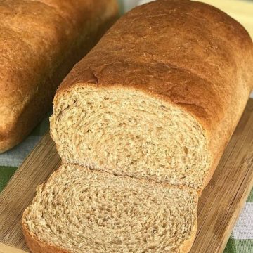 Baked honey wheat bread sliced and laying on a wooden cutting board.