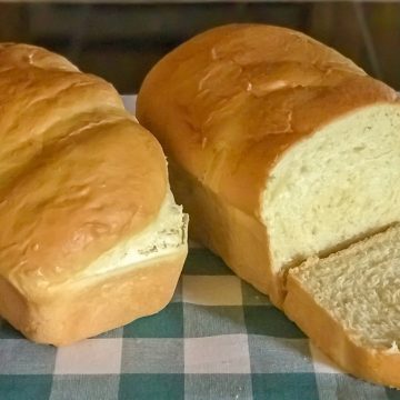 Sliced baked homemade butter bread laying on a blue buffalo check cloth.