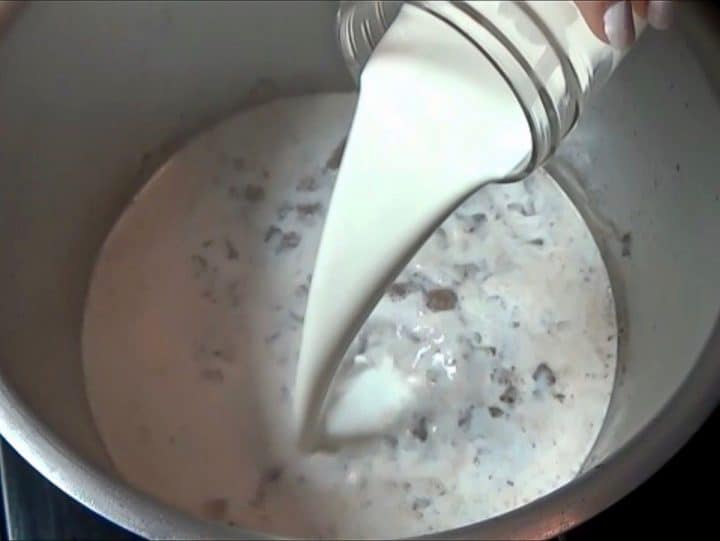 Whole milk in a glass jar being poured into a stock pot.