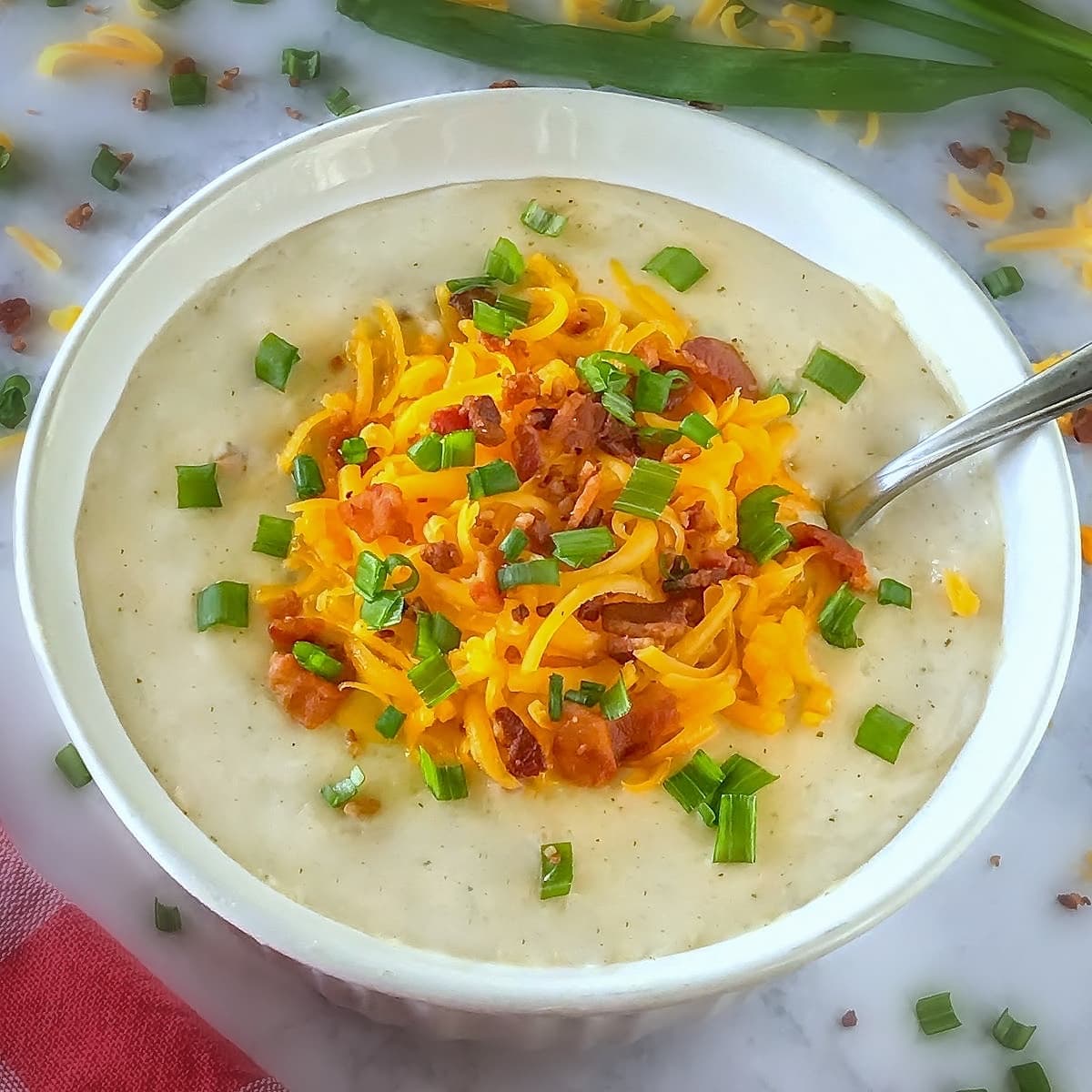 Potato soup in a white bowl with cheese, bacon, and green onions on top.