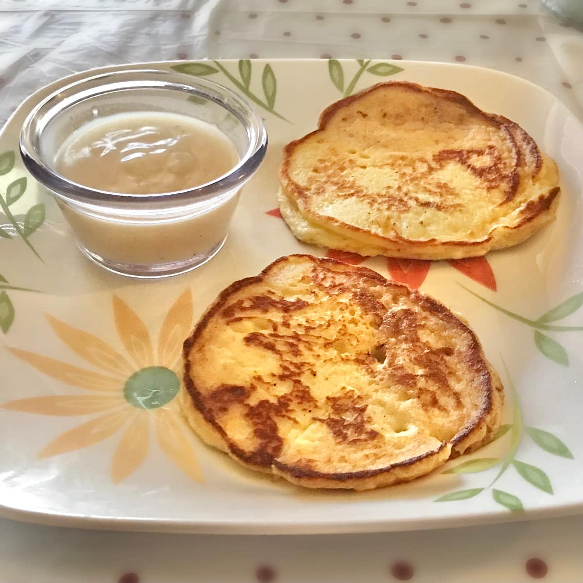 Cooked mashed potato pancakes laying on a white, floral plate with a small clear bowl of white gravy.