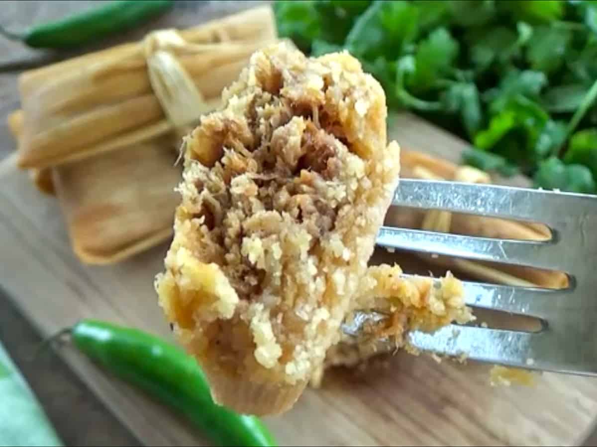 A piece of cooked red chile sauce pork tamales on a silver fork.