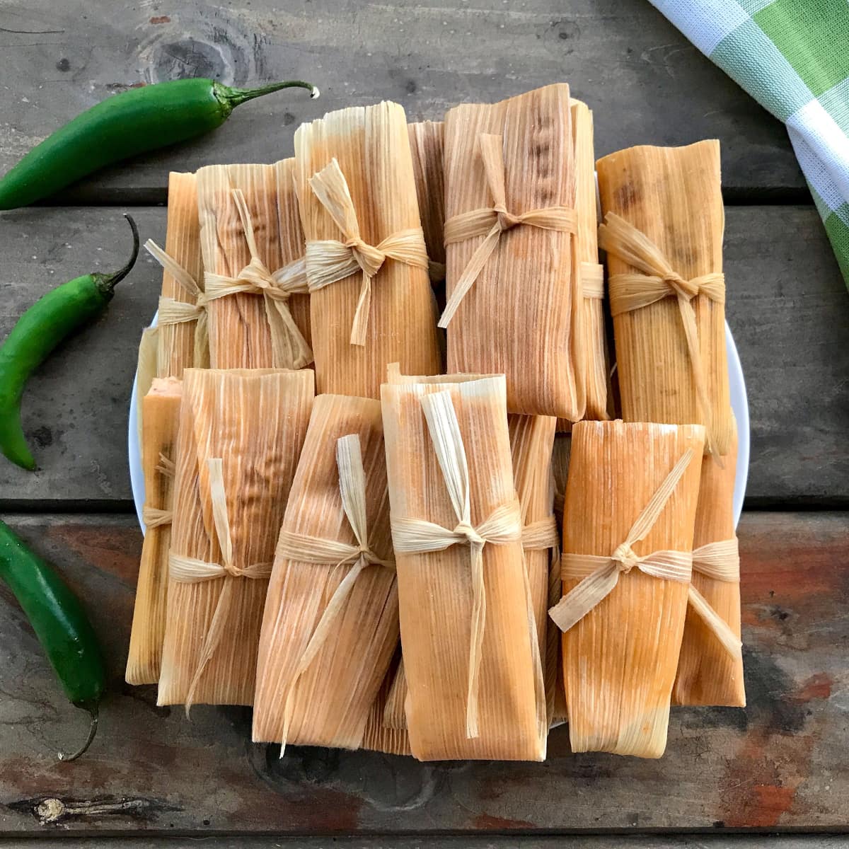 Cooked pork tamales laying on a white plate on top of a wooden table.