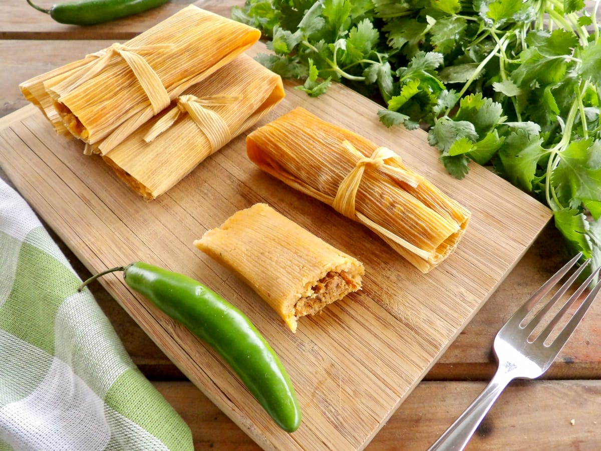 Cooked pork tamales laying on a wooden cutting board on top of a table.