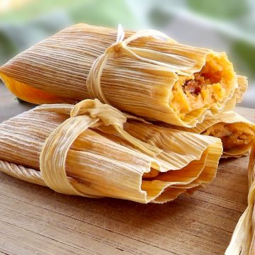 Cooked pork tamales laying on a wooden cutting board on top of a table.