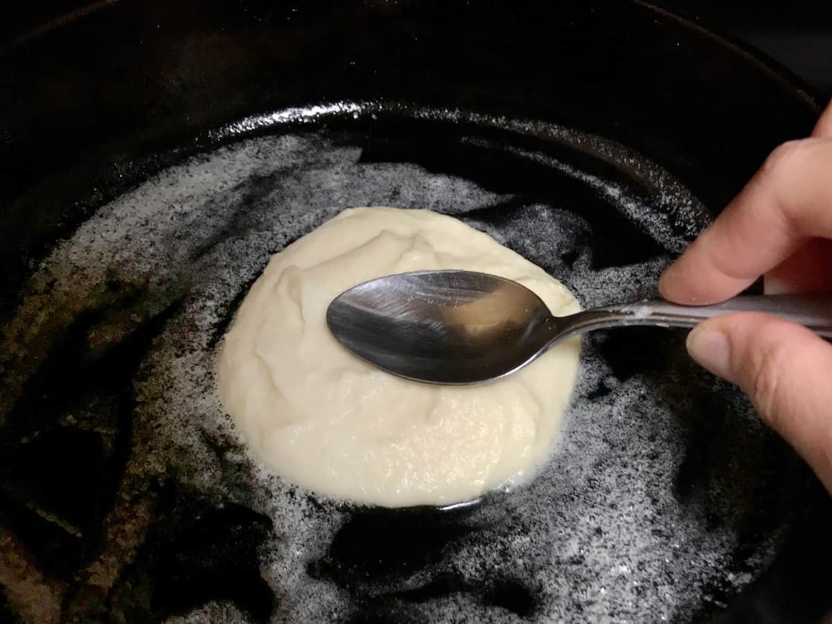 Spooning mashed potato pancake batter onto a cast iron skillet.