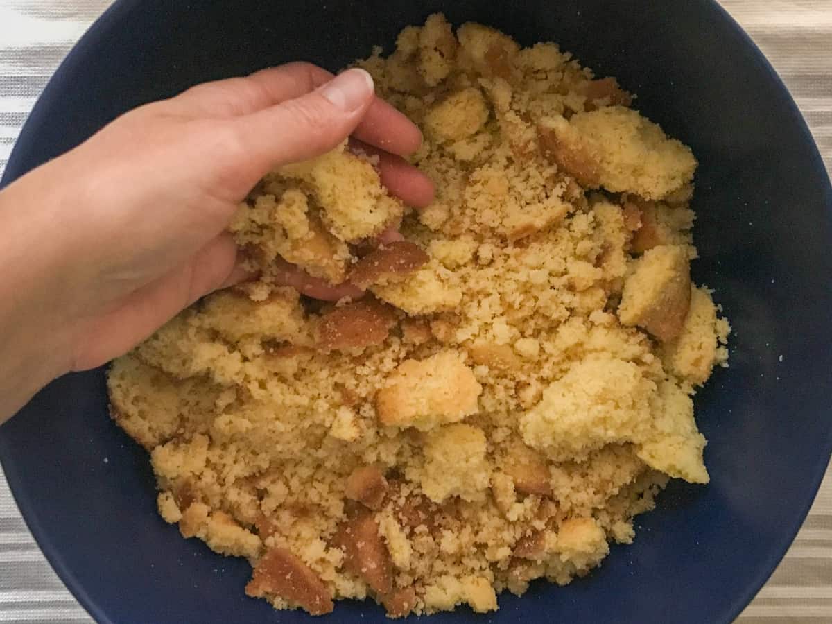 Breaking cornbread muffins up into large chucks in a large blue bowl.