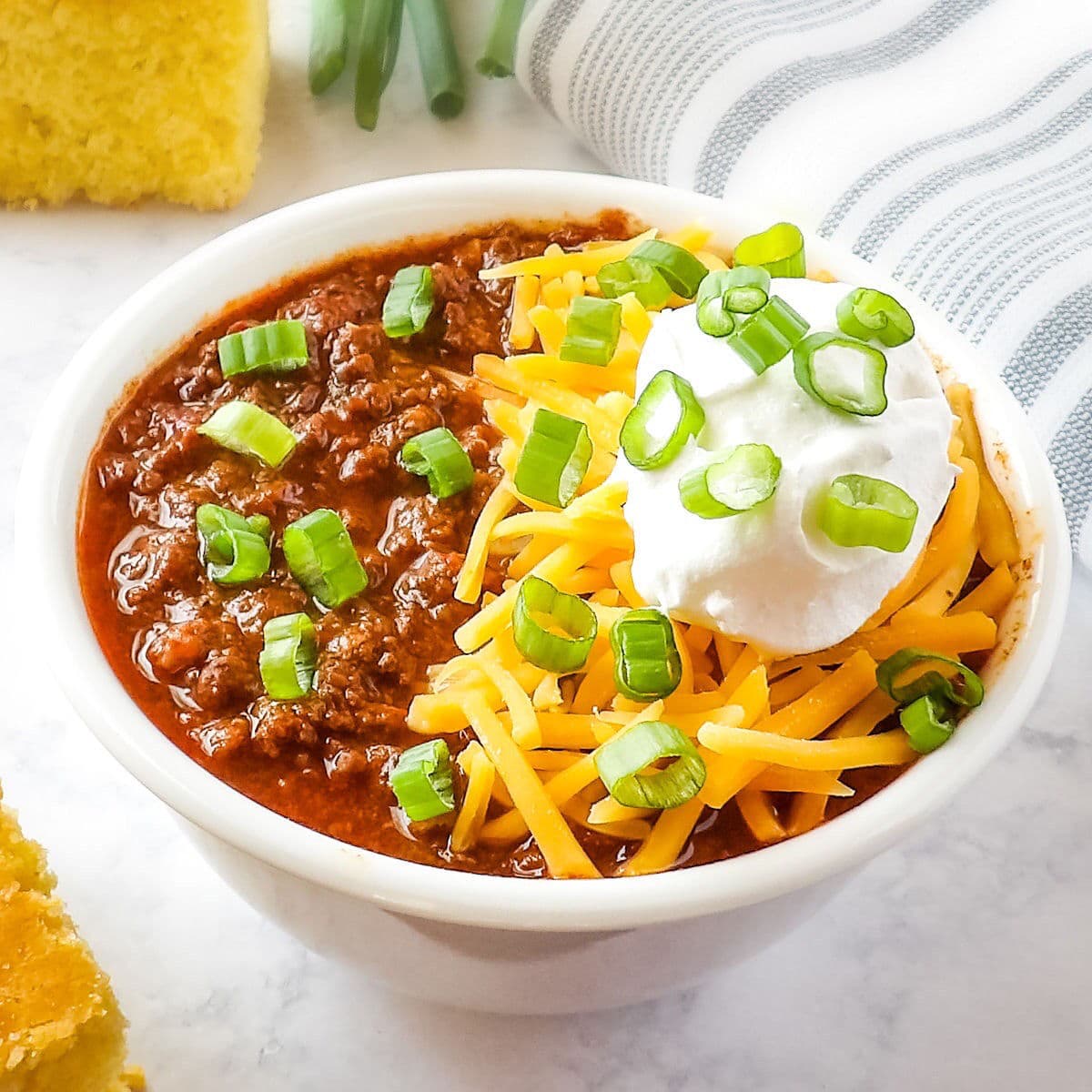 Slow Cooker Venison Chili (deer chili) in a white bowl with cornbread and green onions.