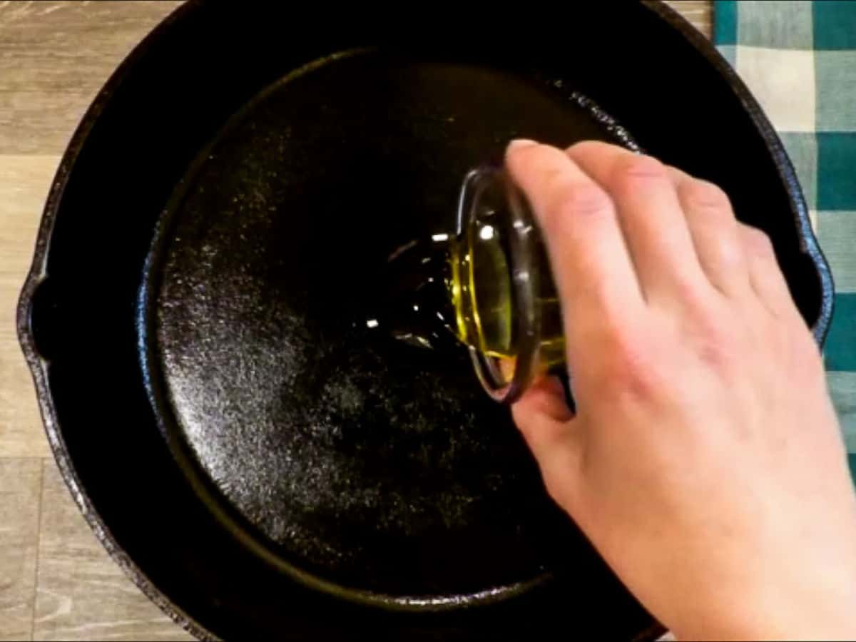 Pouring olive oil into a black cast iron skillet.