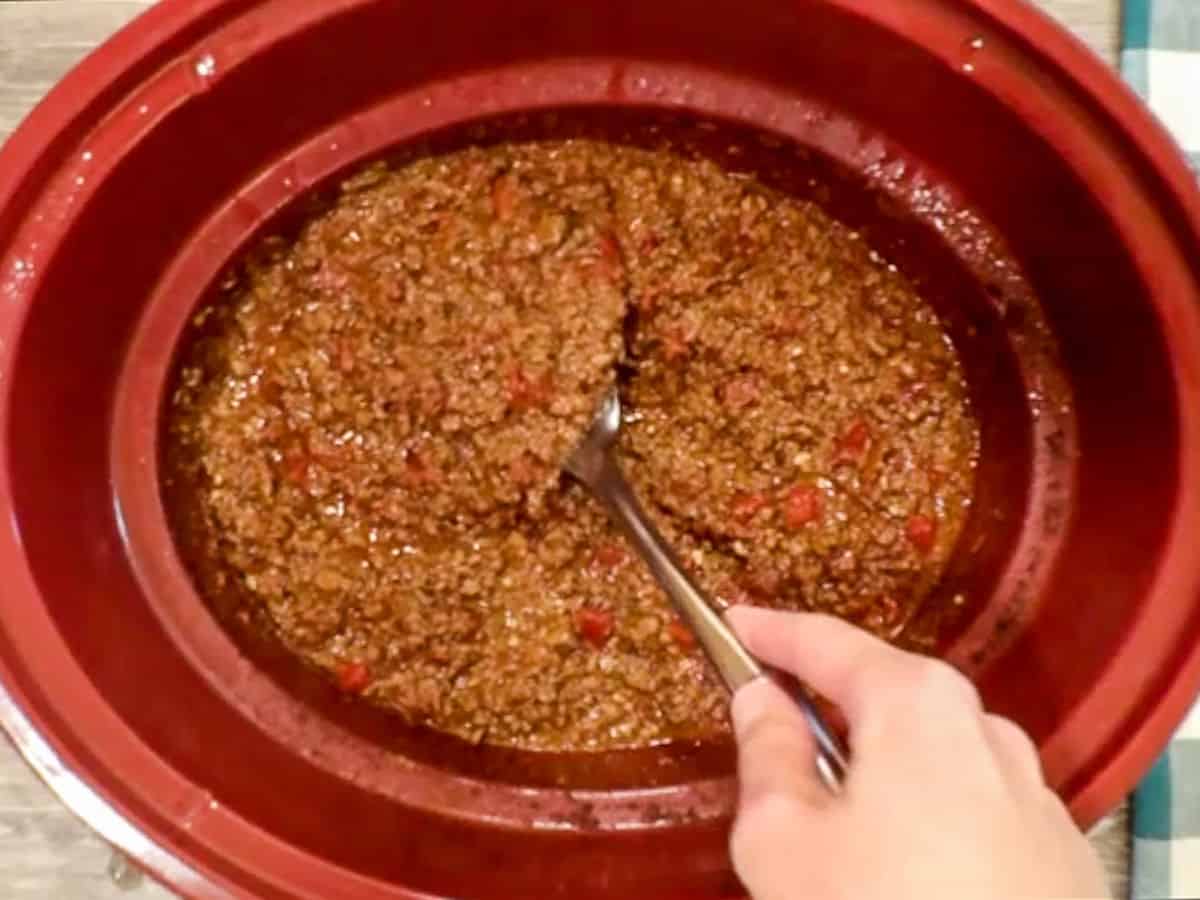 Stirring cooked venison chili in a red crockpot.