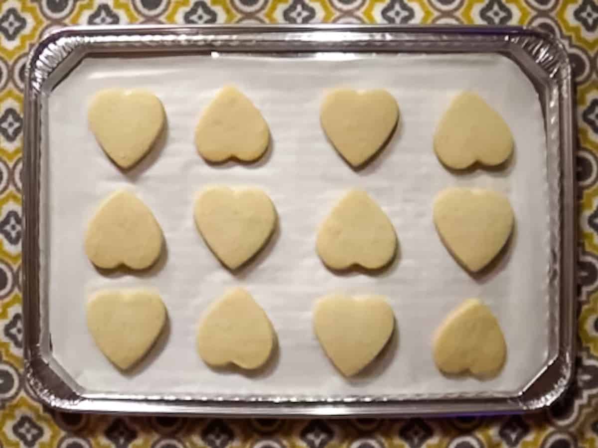 Baked heart shaped sugar cookies laying a baking sheet lined with parchment paper.