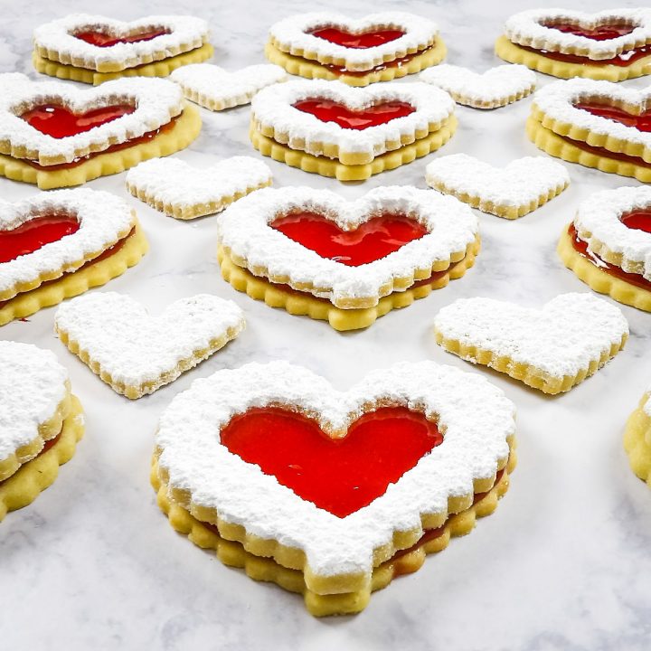 Heart Shaped Linzer Cookies filled with Raspberry Jam laying on marble countertop.