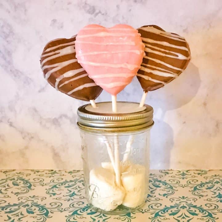 Chocolate Dipped Heart Shaped Sandwich Cookie Pops in a clear mason jar with marshmallows on the bottom.