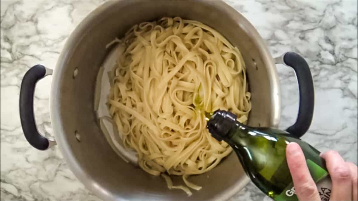 Pouring olive oil into cooked fettuccine noodles before tossing it together.