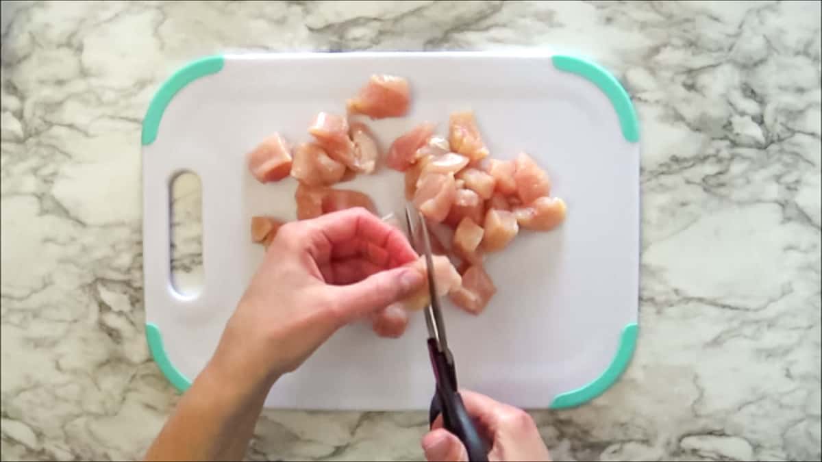 Cutting chicken breasts into 1 inch pieces with kitchen sheers.