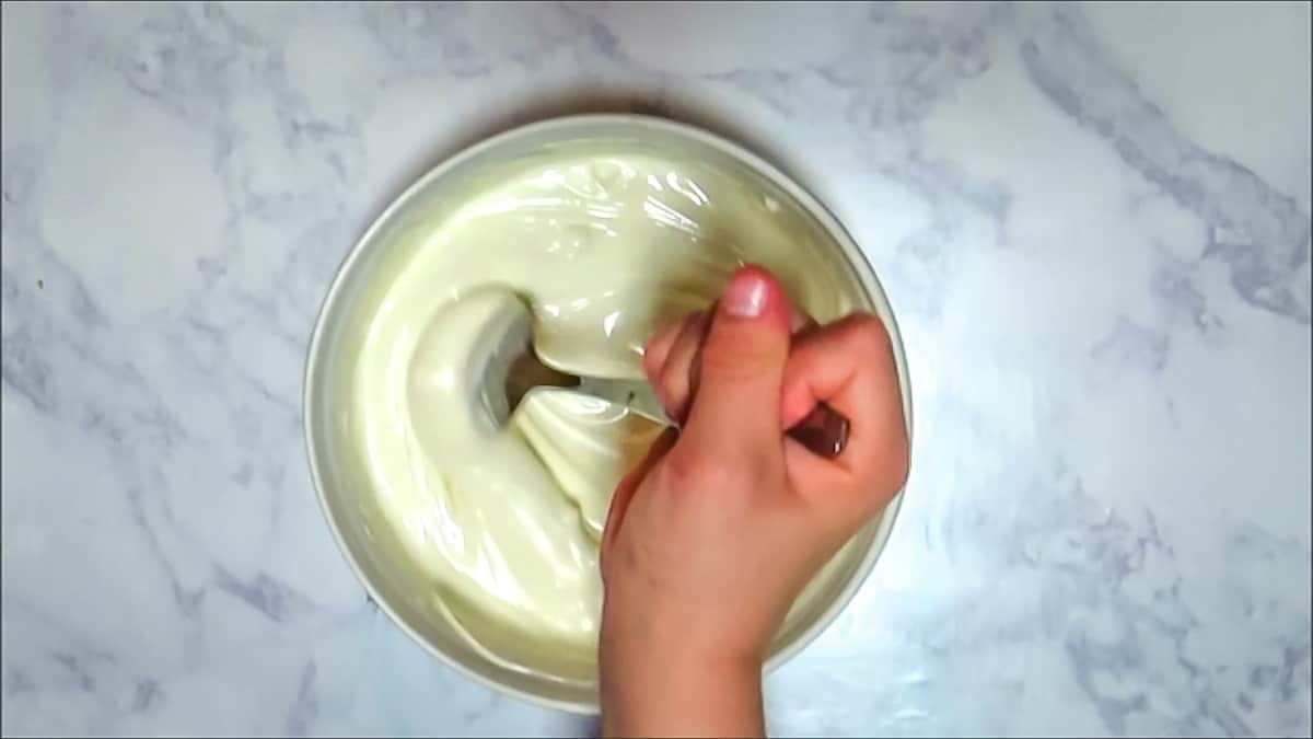 Stirring melted white chocolate with a spoon in a white bowl.