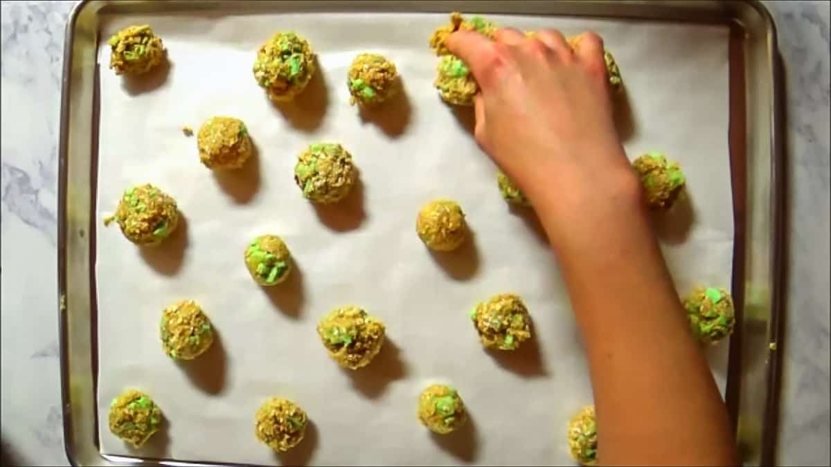 Placing oatmeal cookie dough balls onto a baking sheet lined with parchment paper.