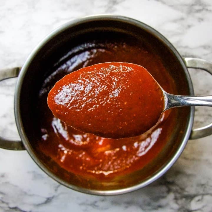 Closeup of homemade barbecue sauce on a spoon with a saucepan in the background.