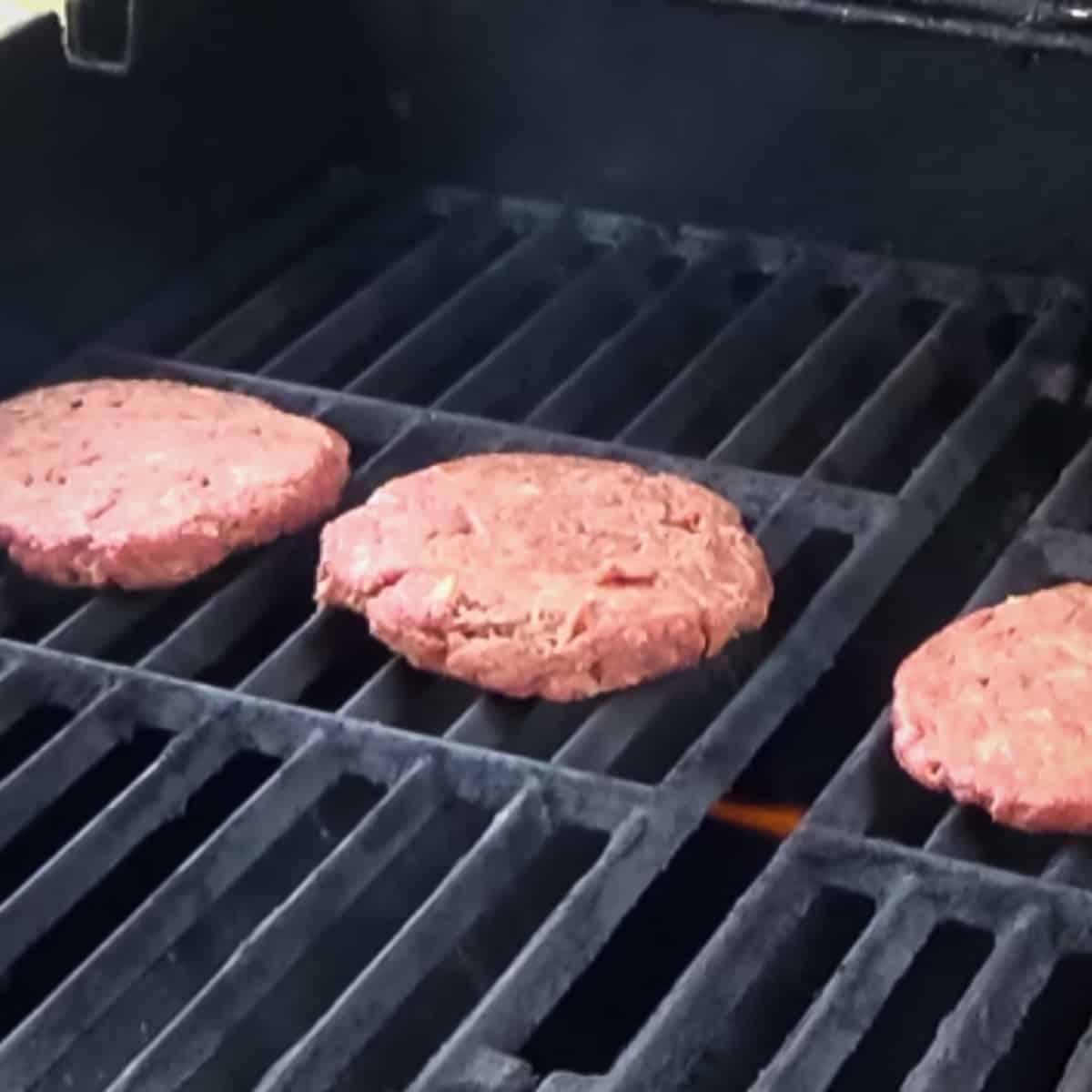 Deer burger patties being cooked on a outdoor gas grill.