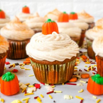 Pumpkin cupcakes with cinnamon cream cheese frosting decorated with candy pumpkins and fall sprinkles.