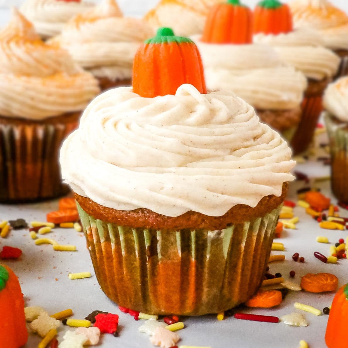 Pumpkin cupcakes with cinnamon cream cheese frosting decorated with candy pumpkins and fall sprinkles.