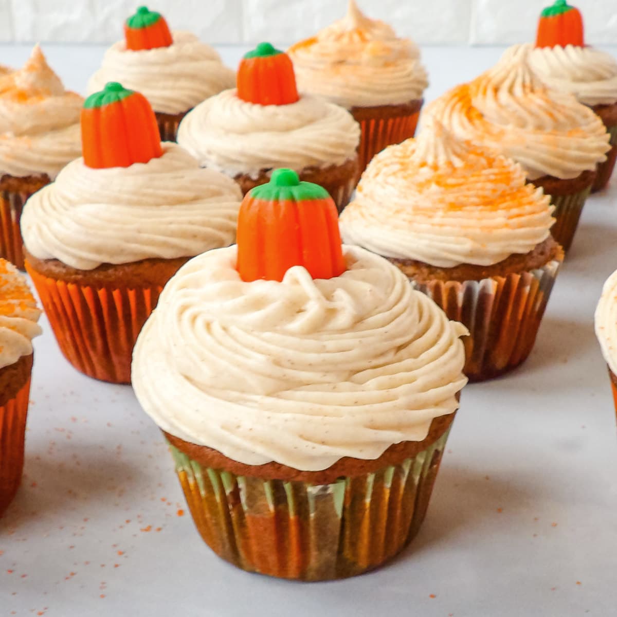 Pumpkin cupcakes with cinnamon cream cheese frosting decorated with candy pumpkins and orange sprinkles.