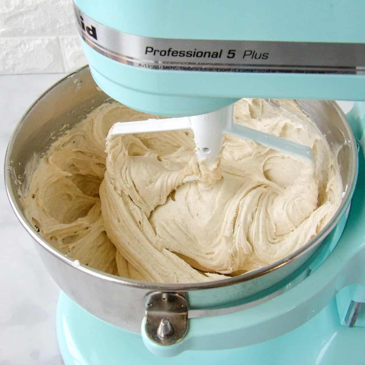 Mixing cinnamon cream cheese frosting in a blue electric stand mixer.