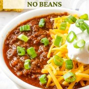 Slow Cooker Venison Chili in a white bowl with cheese, sour cream, and green onions garnished on top.