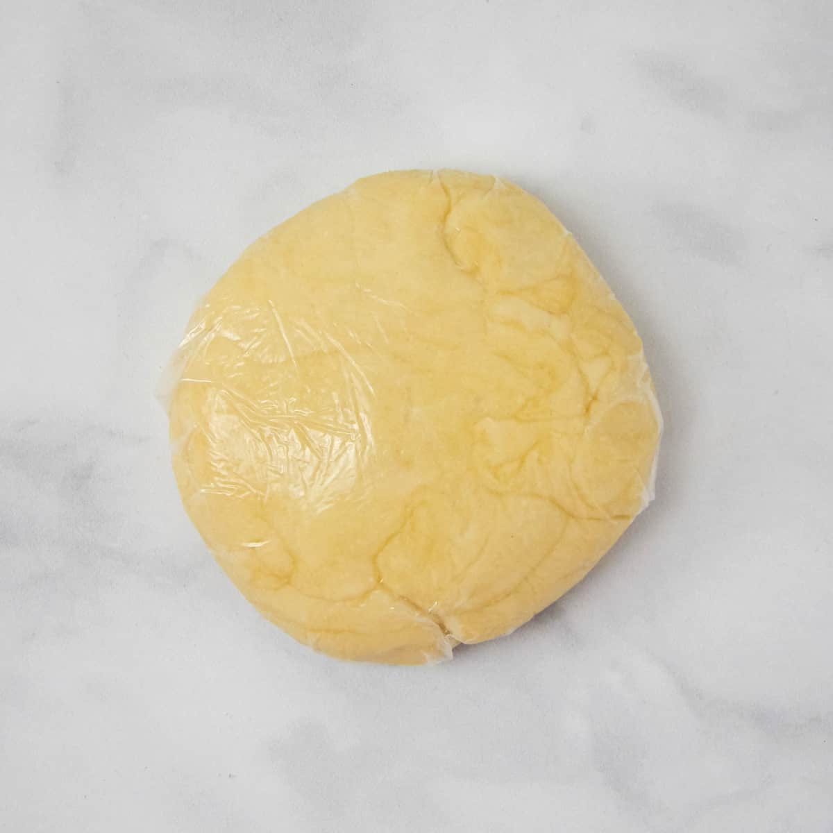 Pie crust dough disk wrapped in plastic wrap.