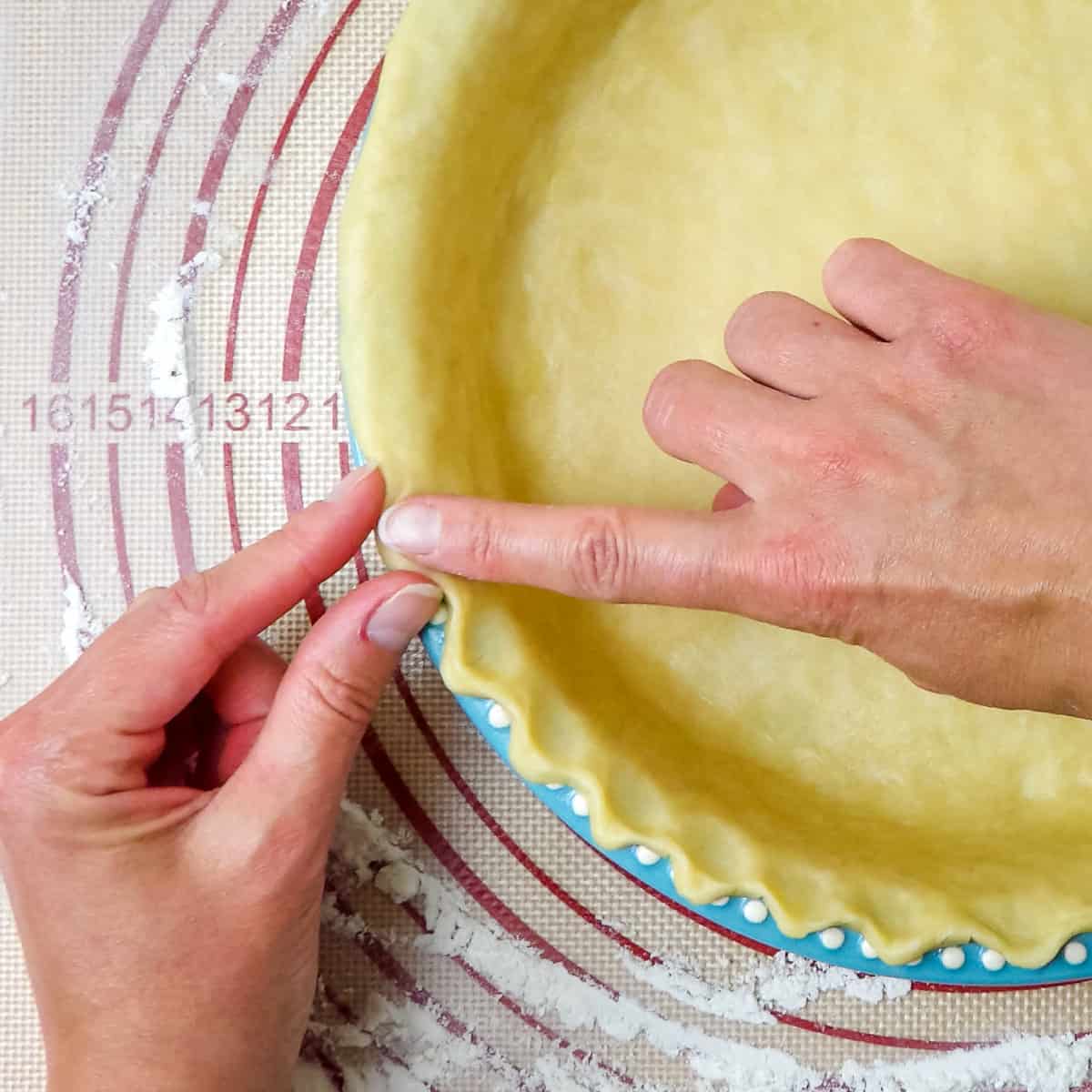 Using fingers to flute the pie crust edge.