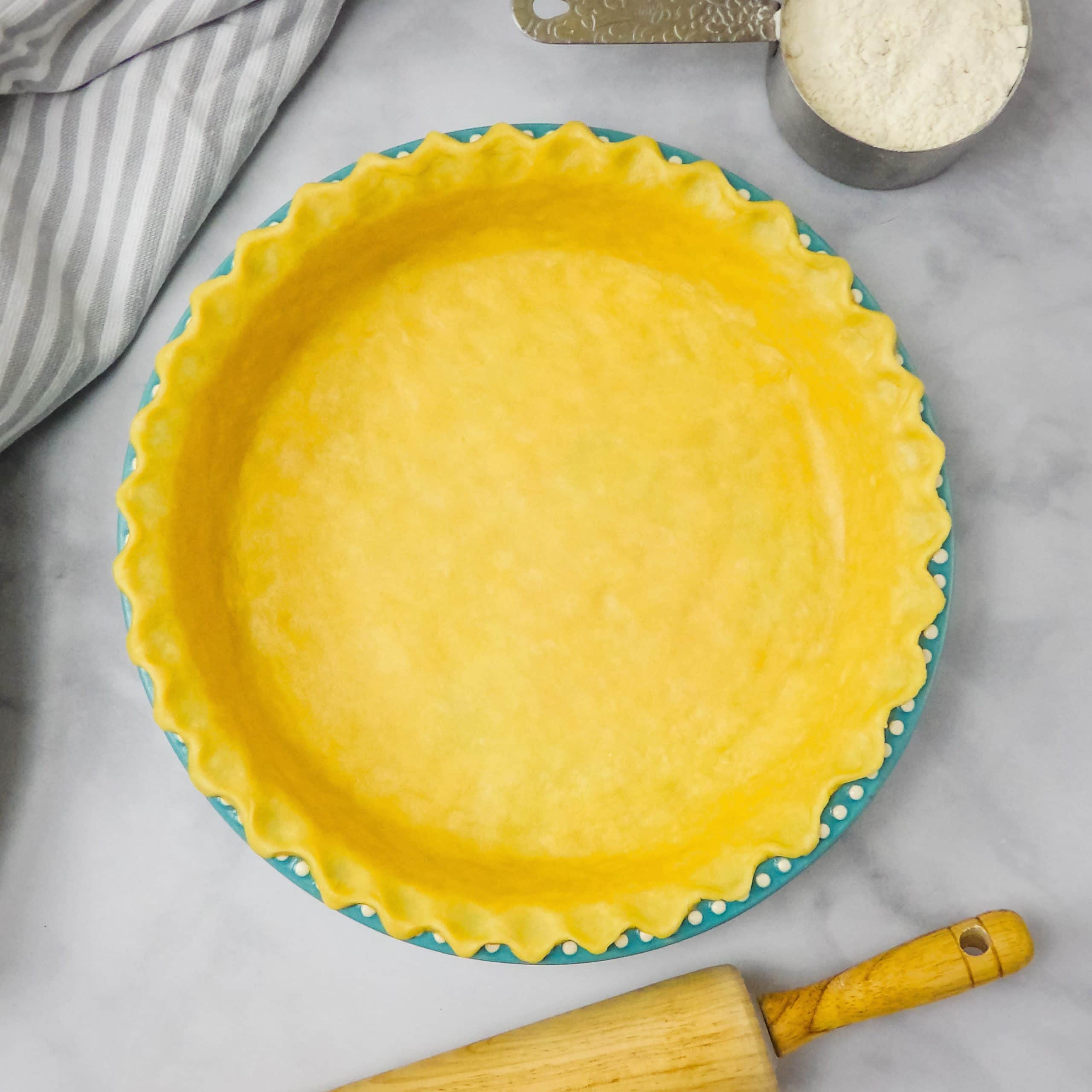 Homemade pie crust dough in a blue pie dish on a white marble countertop.