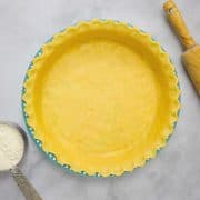 Homemade pie crust dough in a blue pie dish on a white marble countertop.