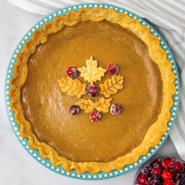 Baked homemade pumpkin pie garnished with pie leaves and sugared cranberries.