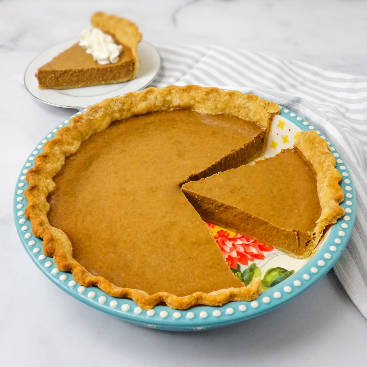 Baked homemade pumpkin pie in a blue pie dish on a white marble countertop.