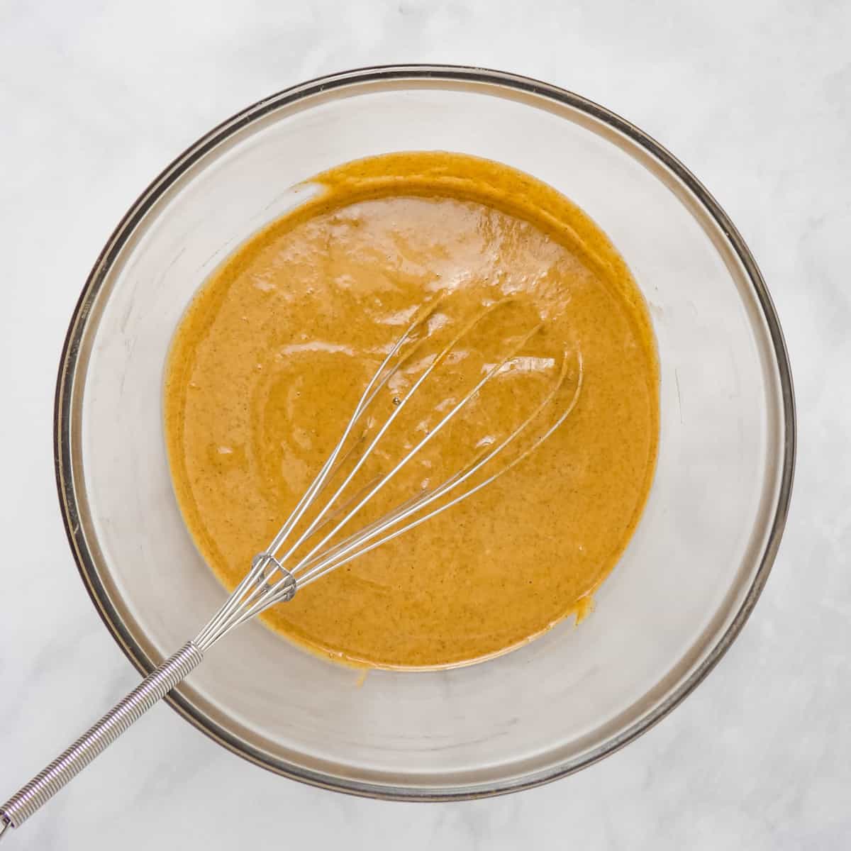 Whisking pumpkin pie filling ingredients together in a large glass mixing bowl.