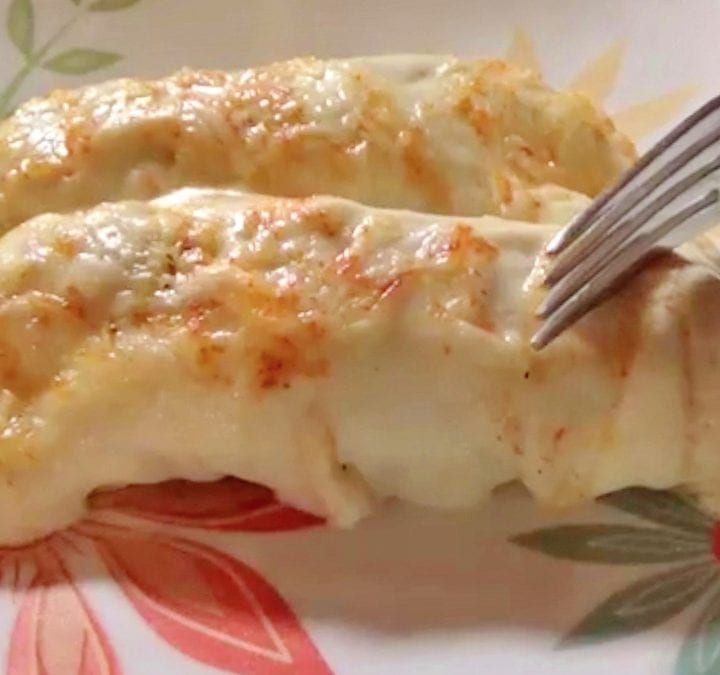 Chicken enchiladas topped with sour cream sauce and cheese laying on a white floral plate.