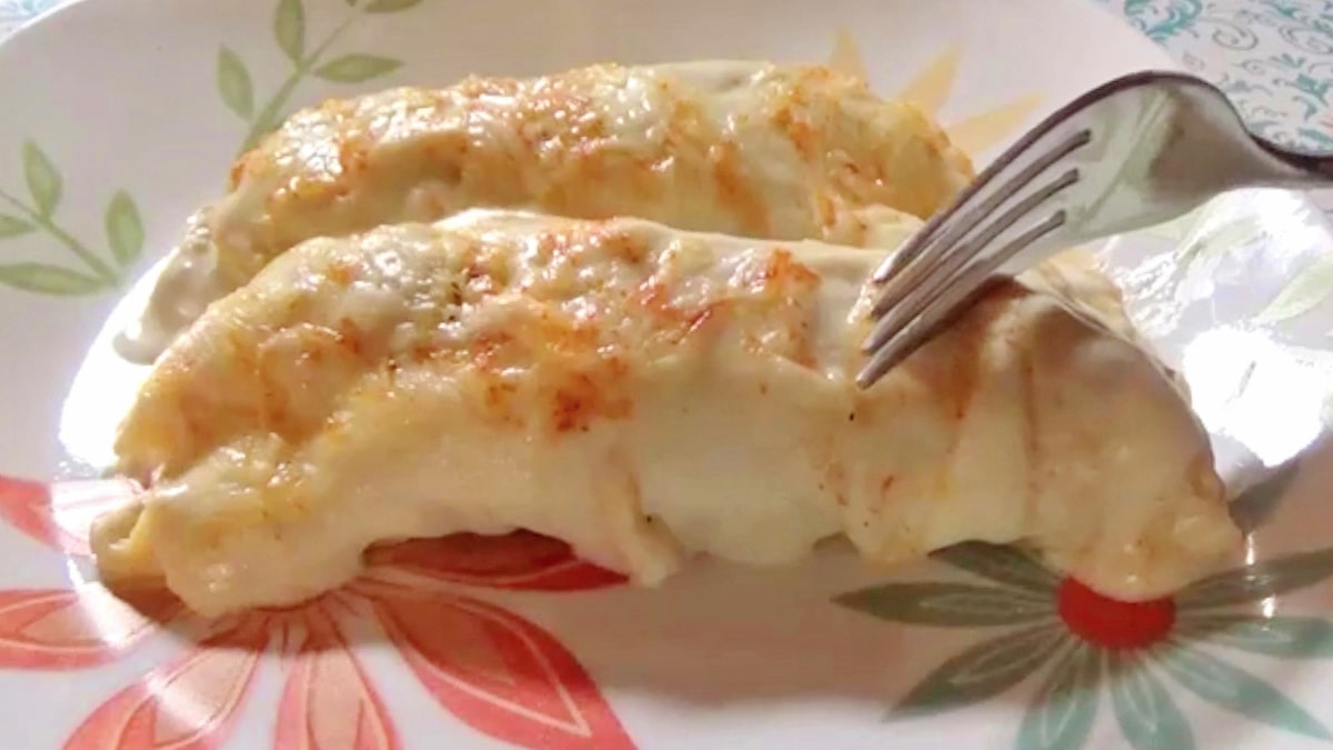 Chicken enchiladas topped with sour cream sauce and cheese laying on a white floral plate.