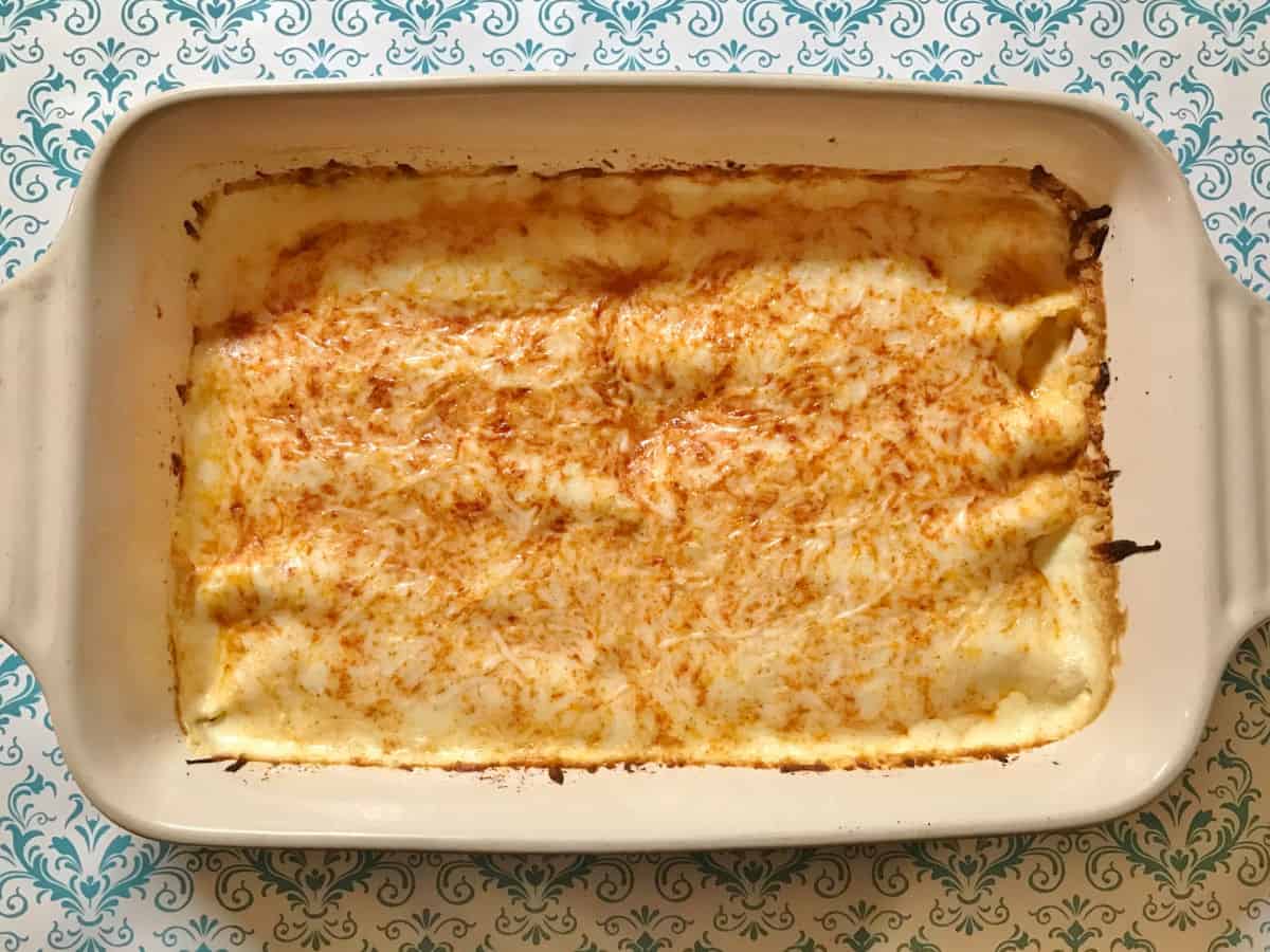 Chicken enchiladas topped with sour cream sauce and cheese in a white casserole dish.
