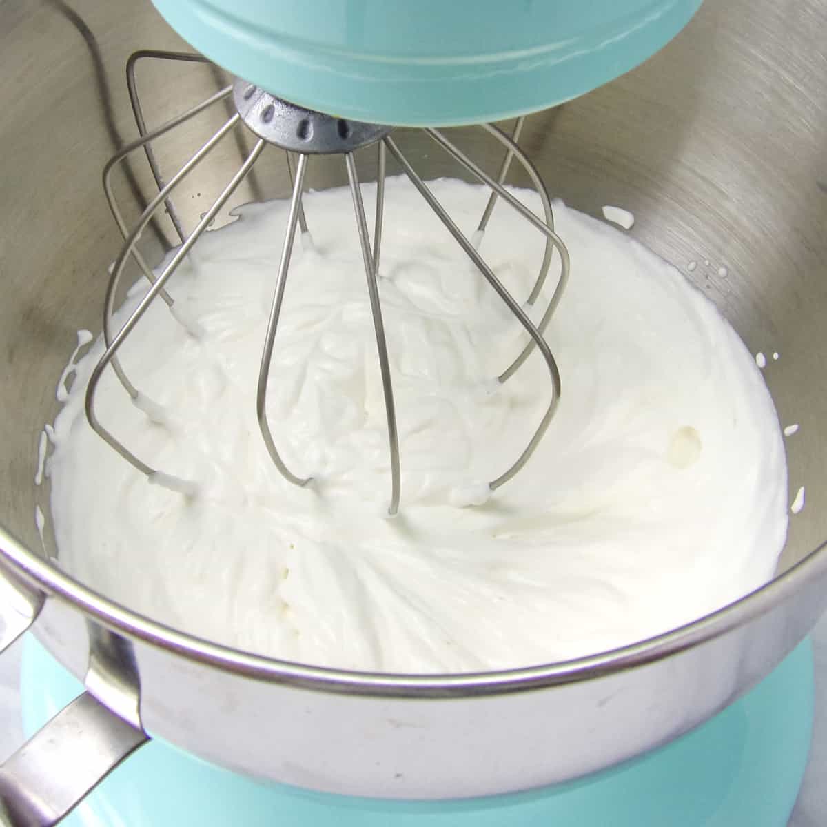 Mixing homemade whipped cream in a blue electric stand mixer fitted with a whisk attachment.