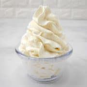 Homemade whipped cream that's been piped into a clear plastic bowl.