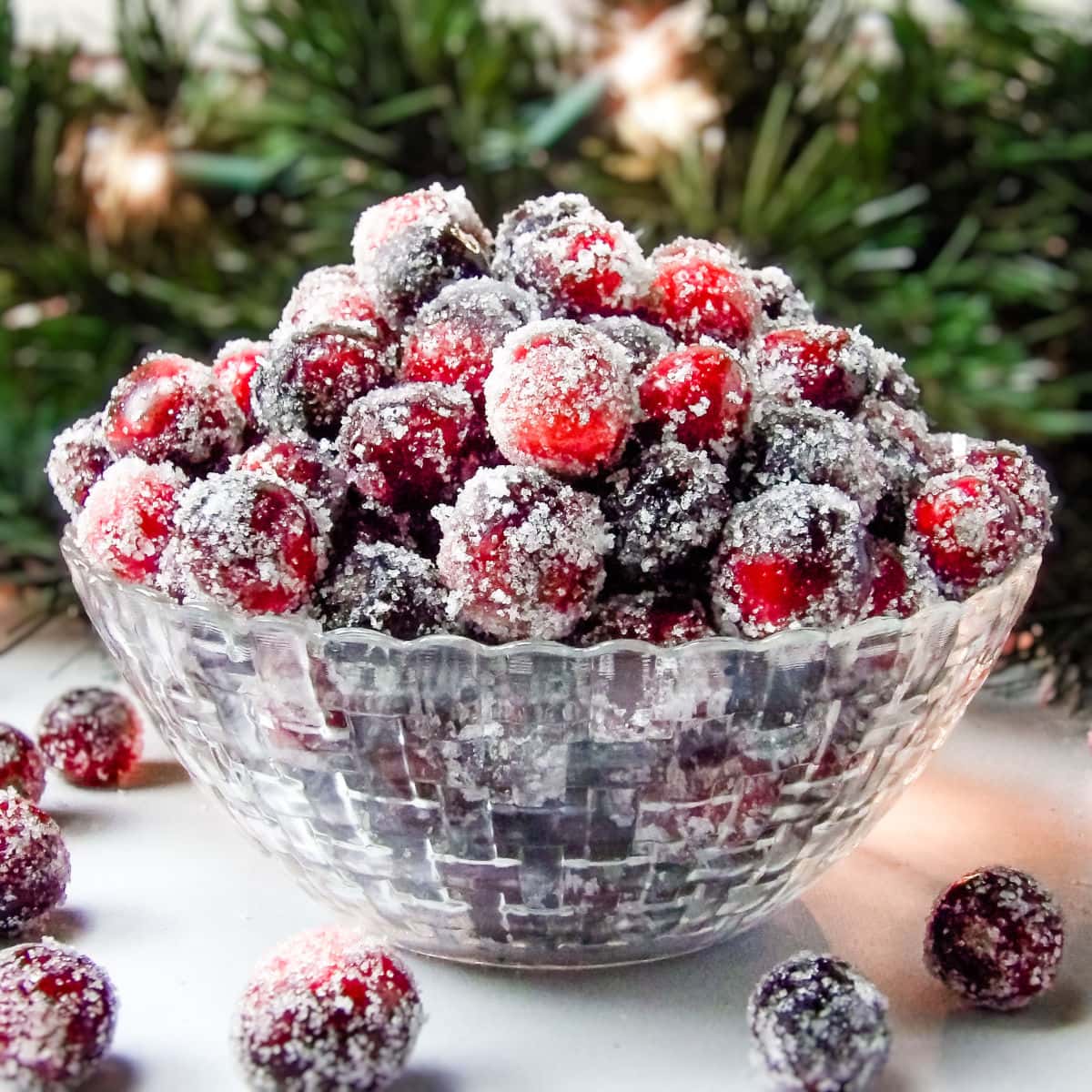 Sugared cranberries in a glass bowl with Christmas garland in the background.