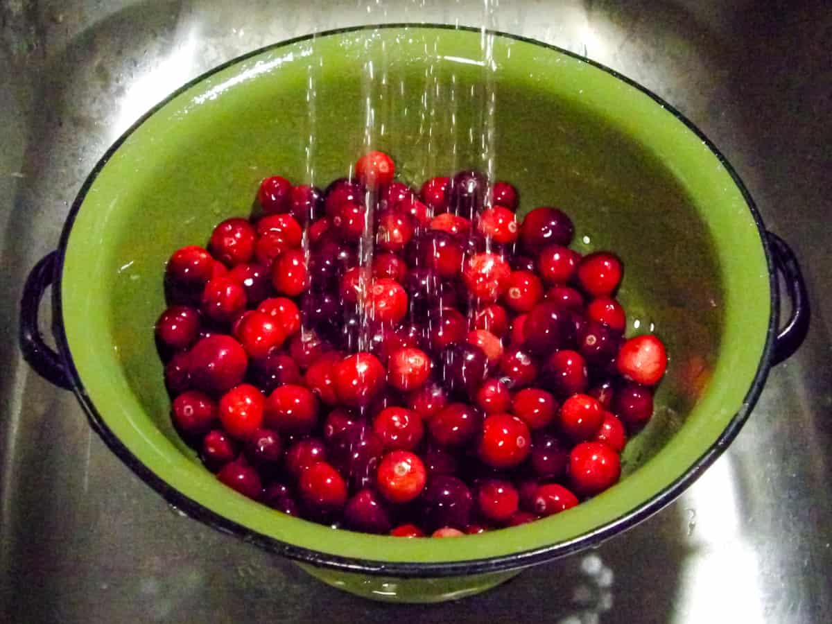 Cranberries being rinsed with water in a green metal strainer.