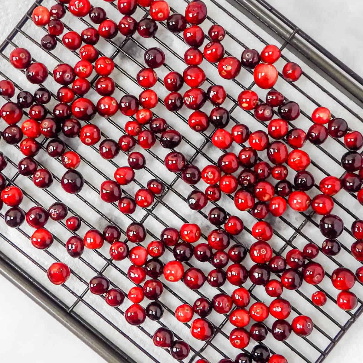Simple syrup coated cranberries drying on a black metal rack.
