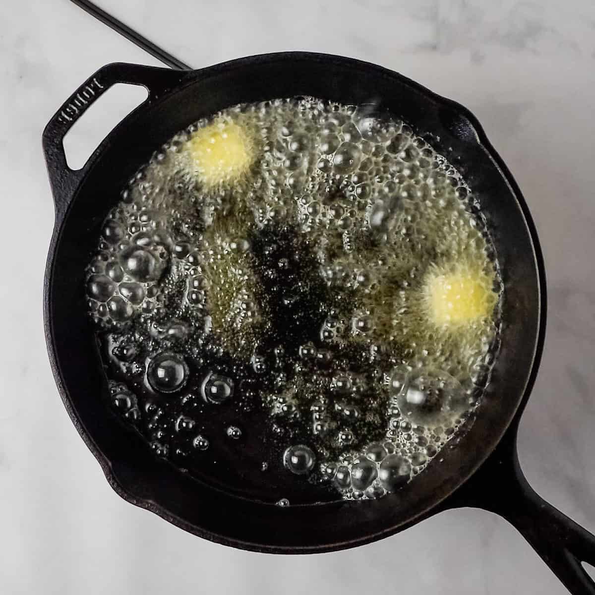 Cooking oil and butter heating up in a cast iron skillet.