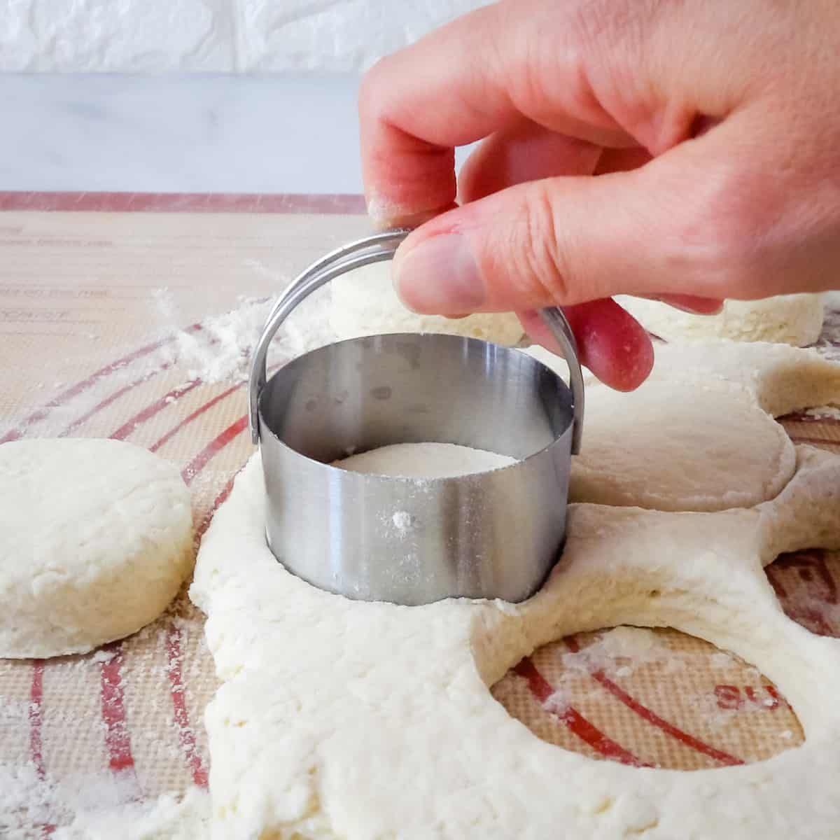 Biscuits being cut out of the dough with a metal biscuit cutter.