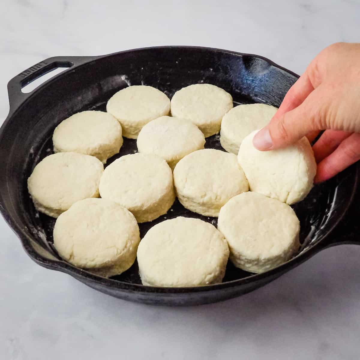Homemade buttermilk biscuits being laid in a cast-iron skillet to bake.